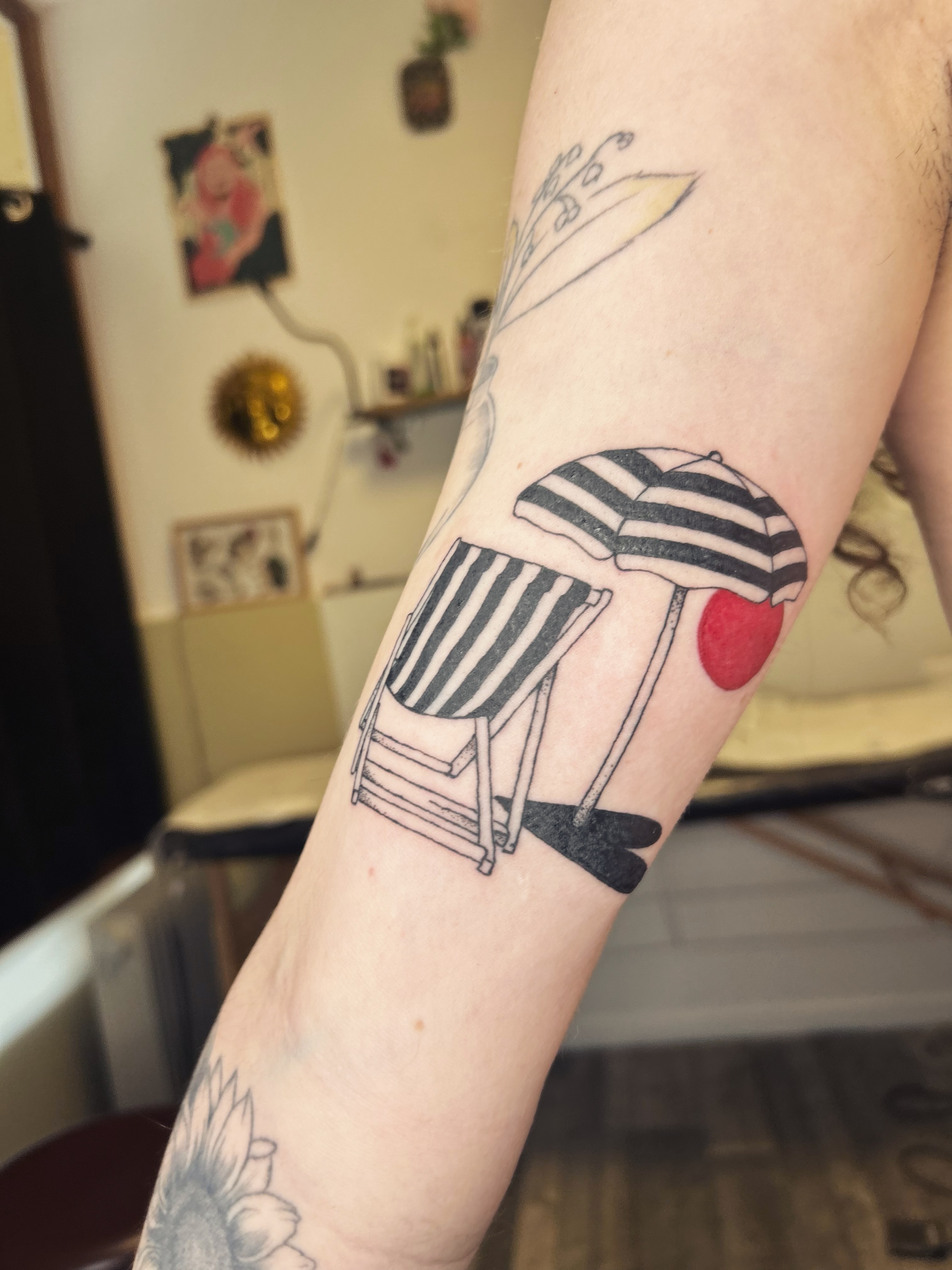Tatouage transat raye et parasol avec un soleil rouge sur l'avant-bras, illustratif noir et gris