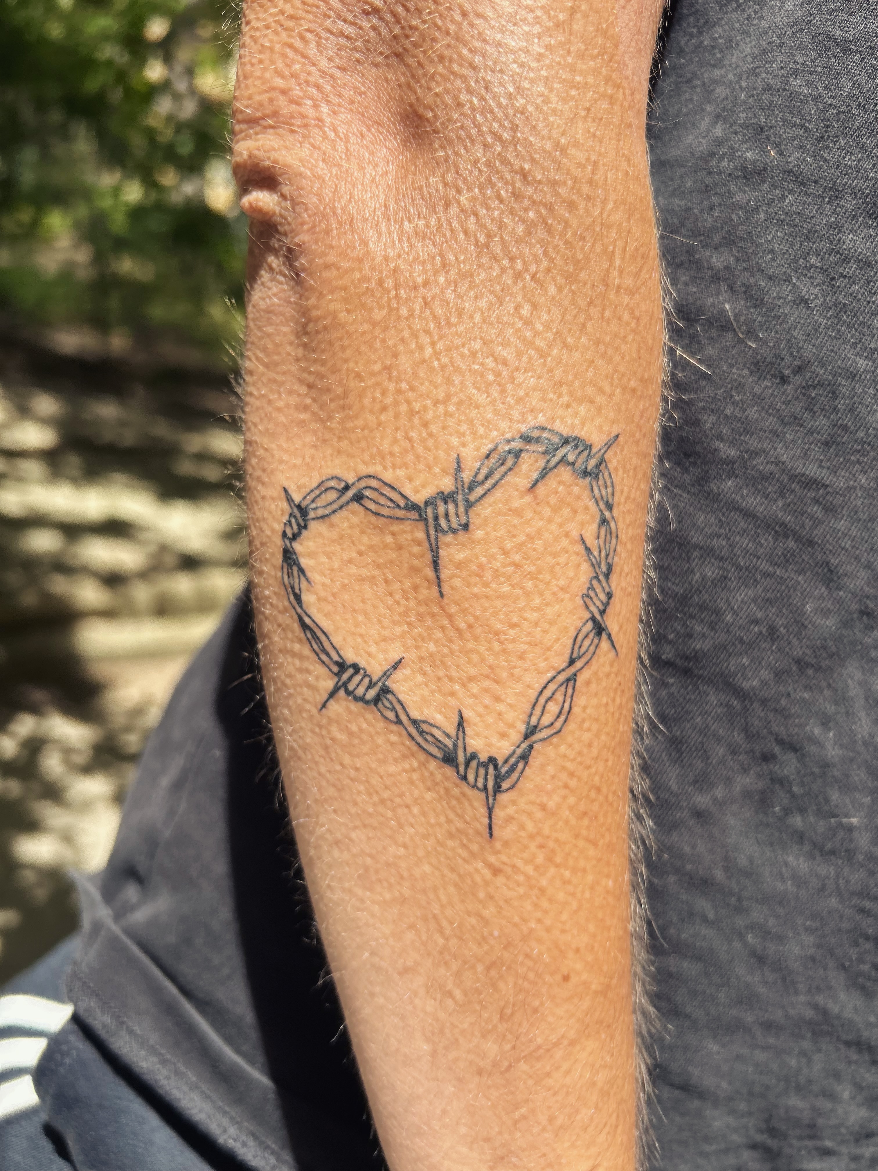 Tatouage coeur en fil barbele sur l'avant-bras, ligne franche
